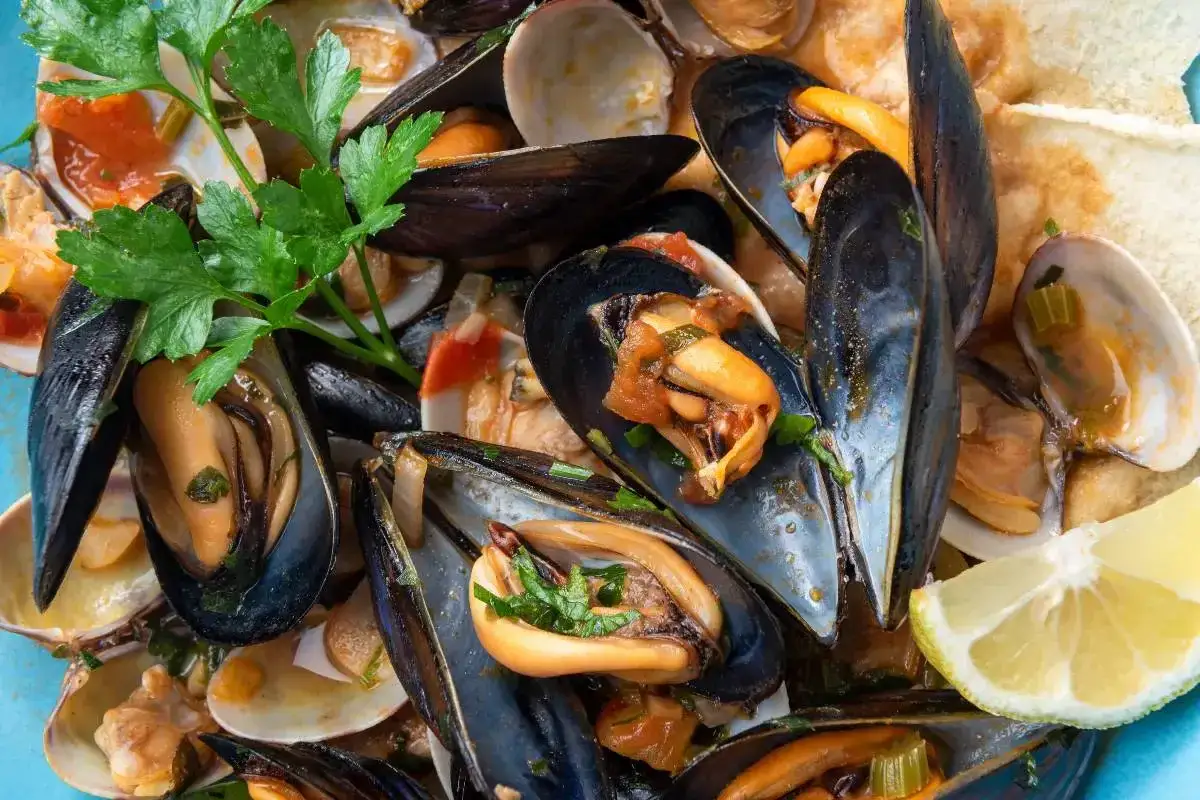 Un invitante saut&egrave; di cozze e vongole, profumato di prezzemolo e servito con fette di pane tostato e spicchi di limone.