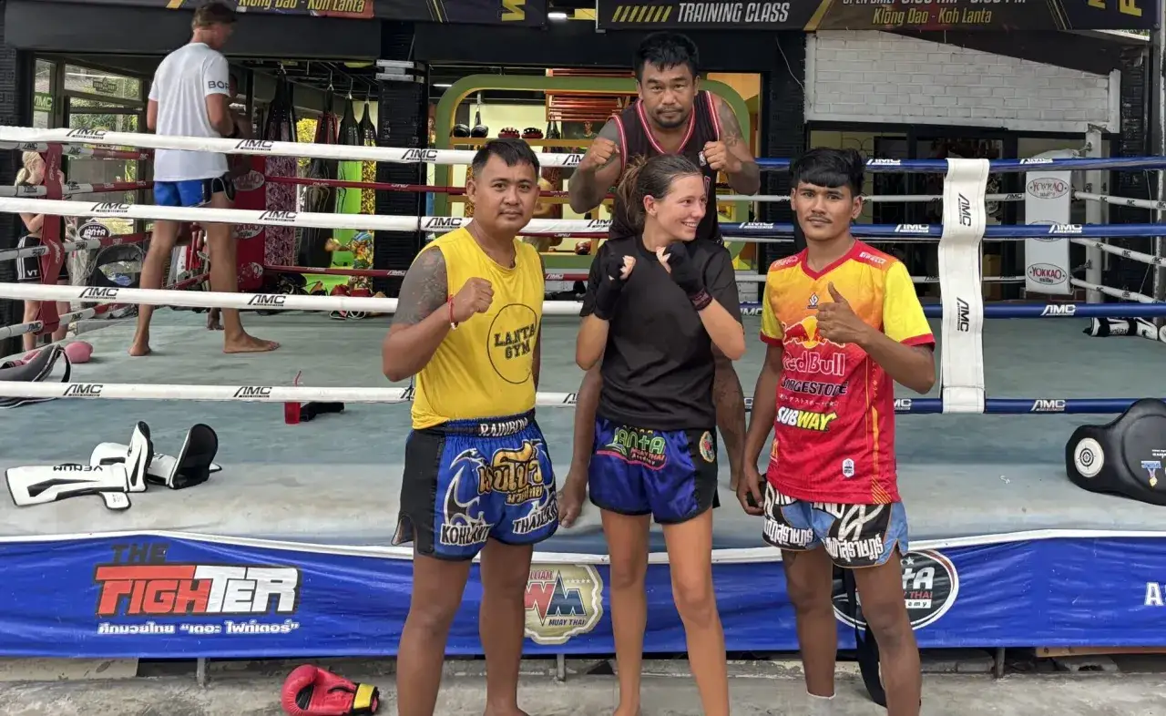 Fyra personer poserar i en ring för c4 thaiboxning. En kvinna i mitten med tränare på var sin sida.