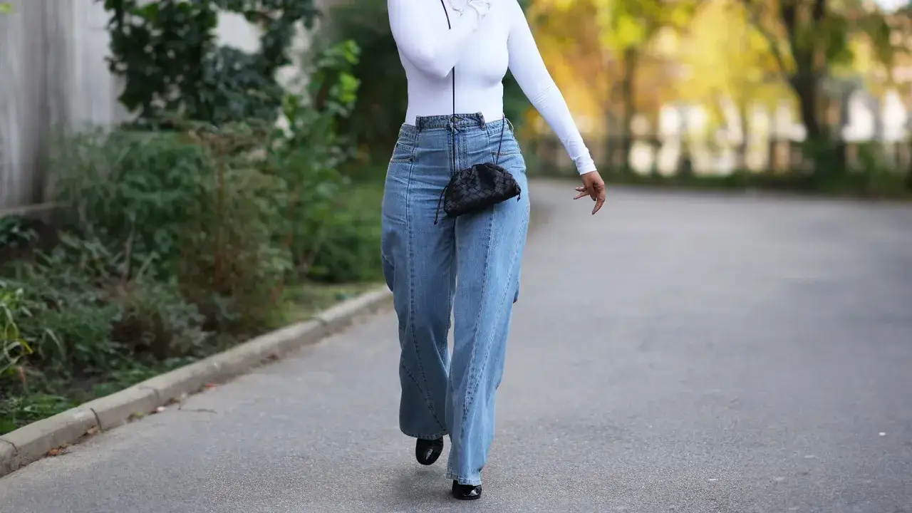 Eleganckie jeansy z wysokim stanem i biały top to świetny sposób, jak ukryć brzuch stylizacje. Czarna torebka dodaje szyku.
