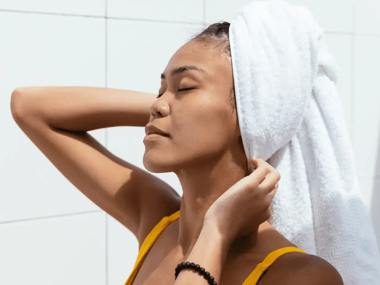 Frau mit Handtuch auf dem Kopf, genießt die Pflege. Ein Leave-in Conditioner macht das Haar geschmeidig.