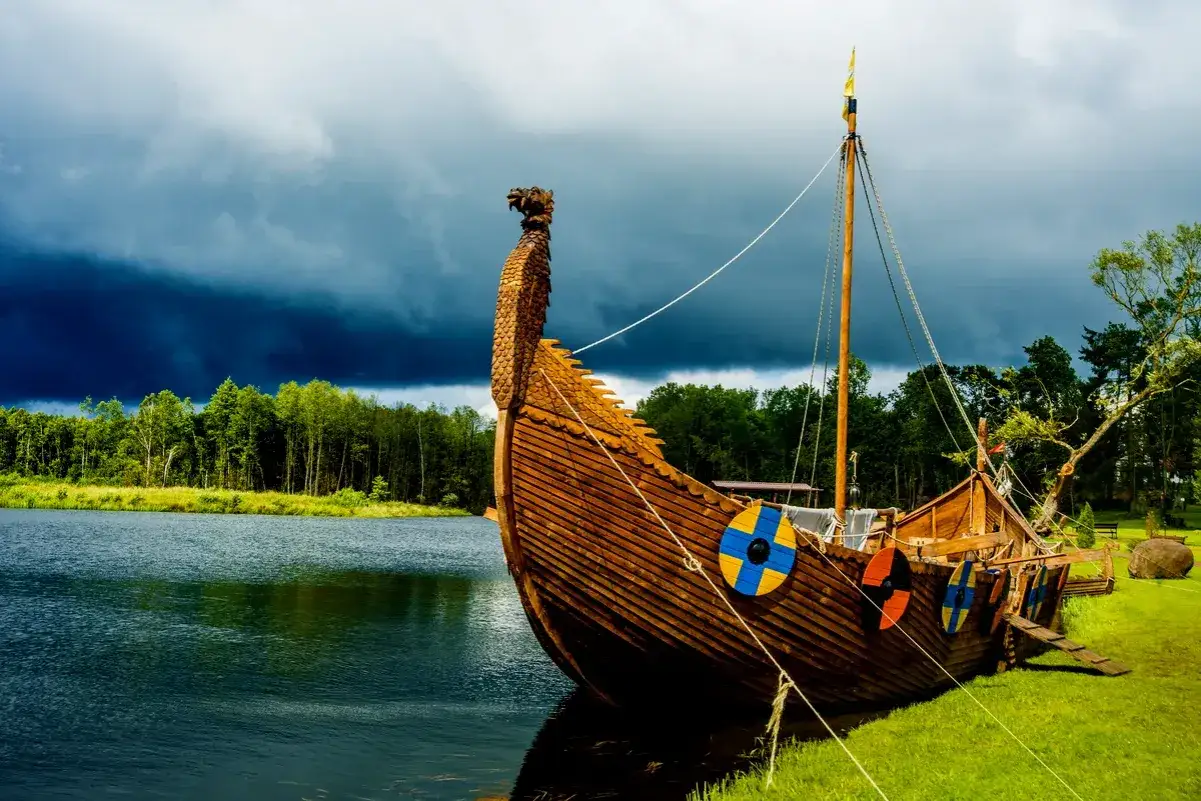 En ståtlig svensk vikingaskepp med drakhuvud vid en sjö, redo för äventyr under mörka moln.