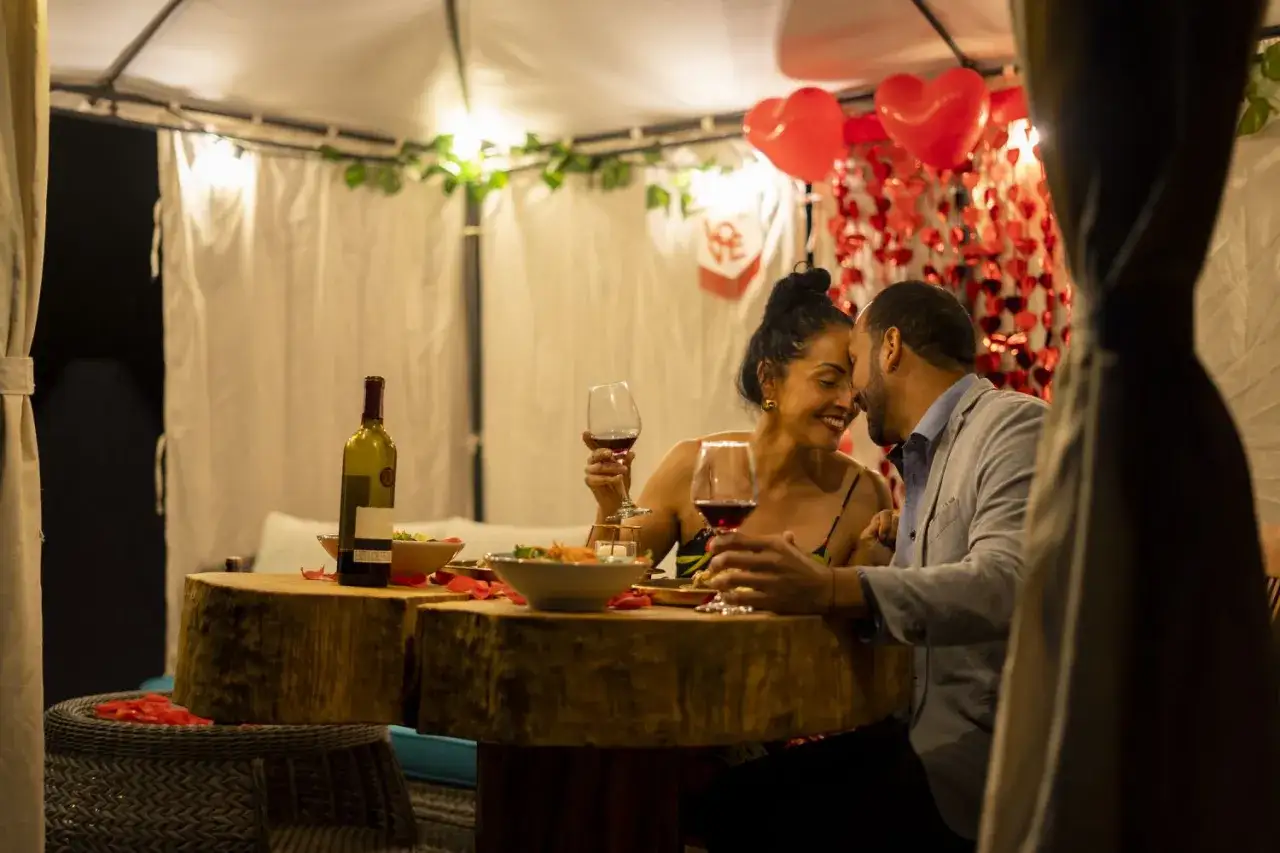 Coppia felice celebra nozze anniversari con cena romantica, vino e cuori rossi.