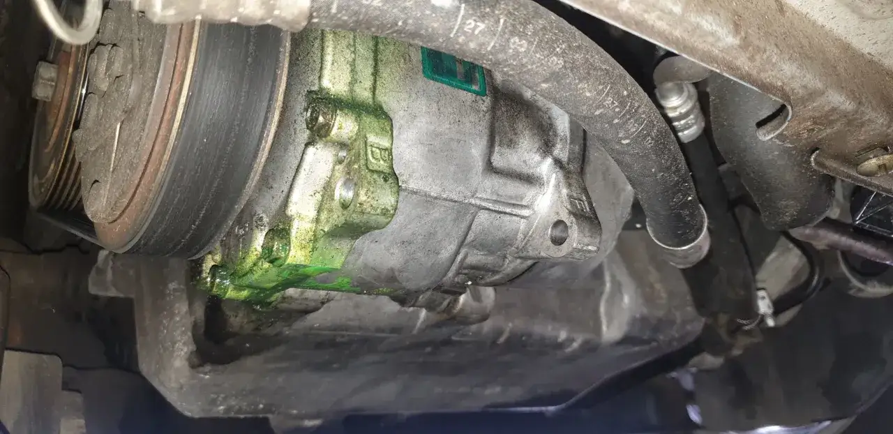 Fuite climatisation voiture : liquide vert vif s'échappe du compresseur, signe d'un problème à réparer.