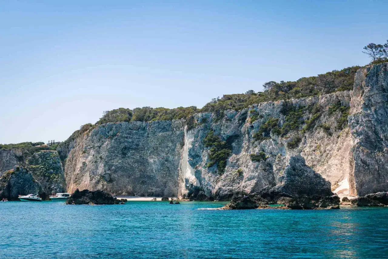 Scogliere imponenti e mare cristallino alle Isole Tremiti. Un piccolo paese si intravede tra la vegetazione lussureggiante che ricopre le rocce.