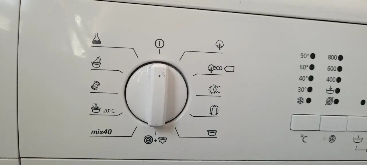 Panel de control de lavadora con varios símbolos: matraz, ropa en tina, ovillo de lana, tina con agua, árbol, eco, sol/luna, camisa, tina vacía. Incluye temperaturas y centrifugado.