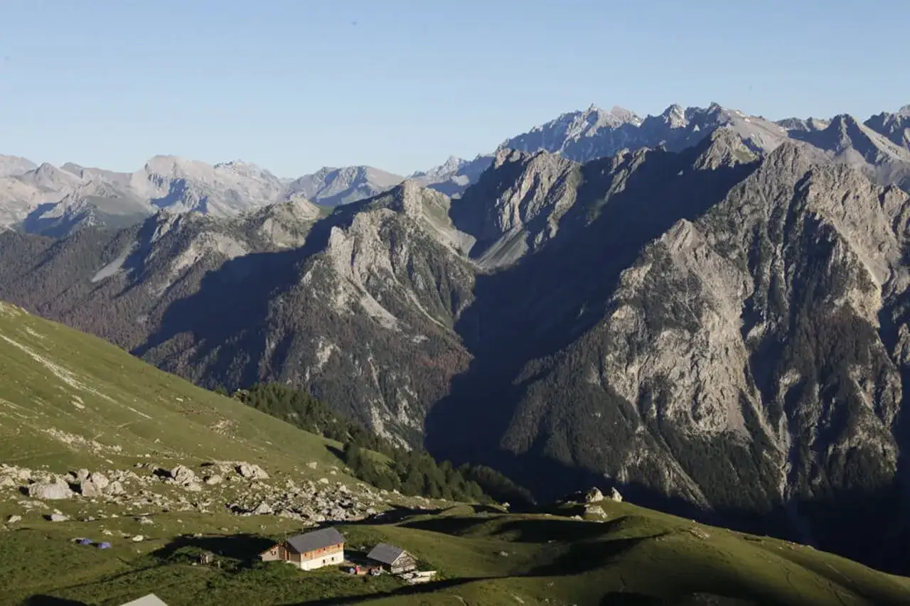 Vue panoramique des montagnes du Queyras, avec des chalets et des tentes sur une pente herbeuse. Un paysage id&eacute;al pour un tour du Queyras 4 jours.