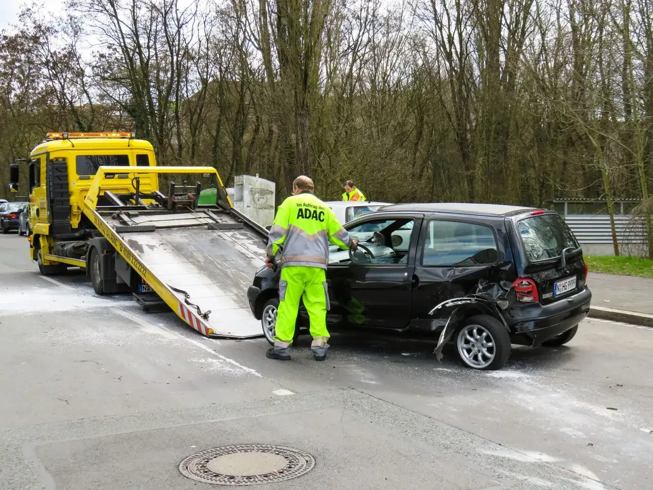 Pomoc drogowa uniqa assistance: żółta laweta ładuje uszkodzone czarne auto po wypadku.