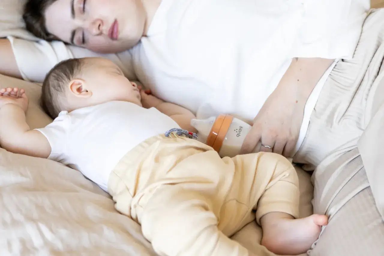 Madre e hijo duermen juntos, con un biberón cerca. Tomas nocturnas bebé 1 mes.