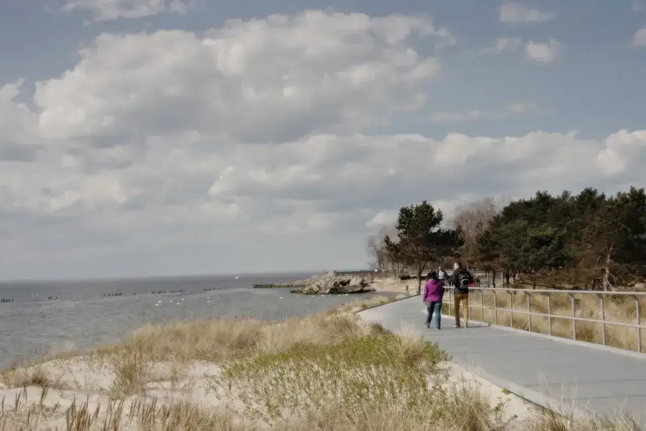 Spacer po plaży, idealne miejsce gdzie nad morze z niemowlakiem. Dwie osoby idą ścieżką przy wydmach.