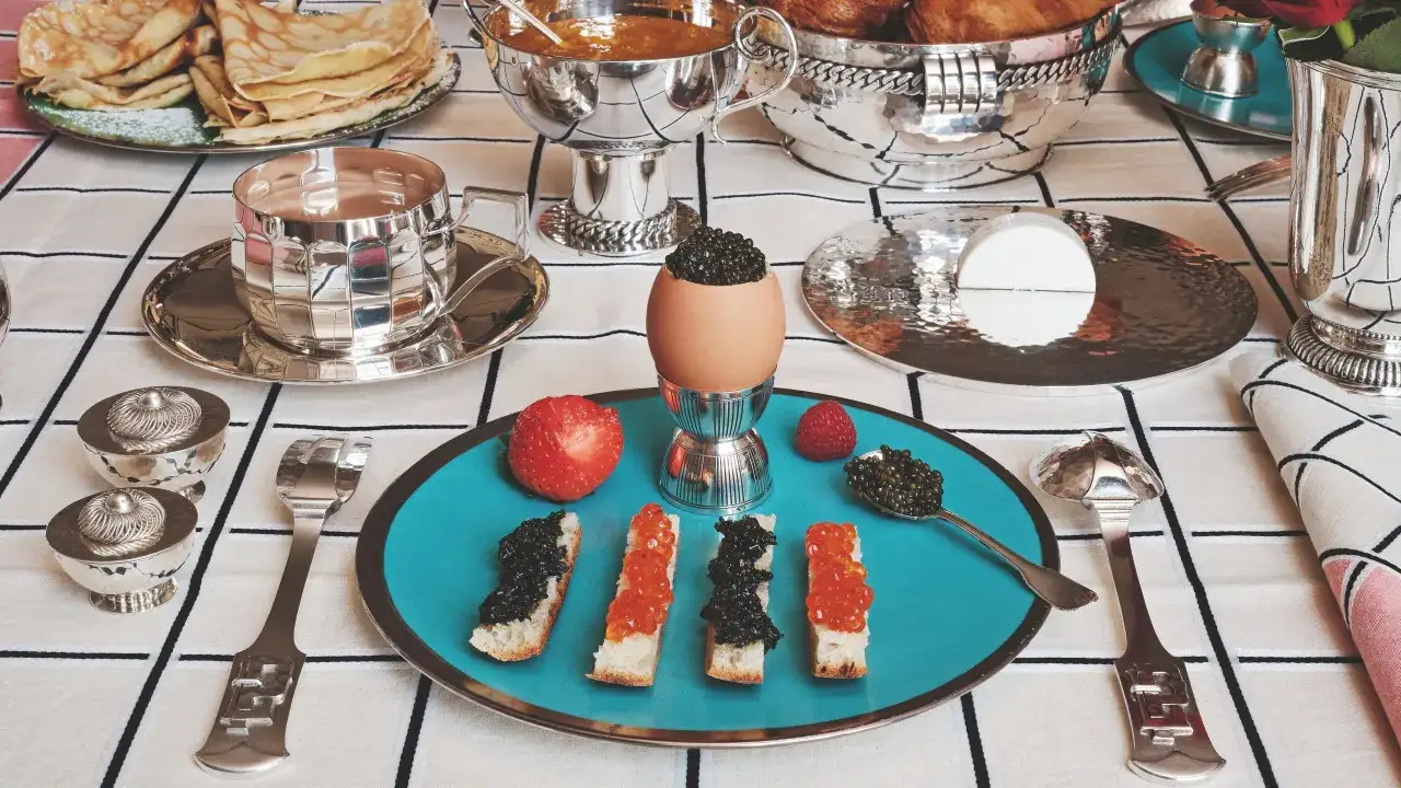 Un service de table à la française élégant pour un petit-déjeuner luxueux : œufs, toasts au caviar, fruits et crêpes.