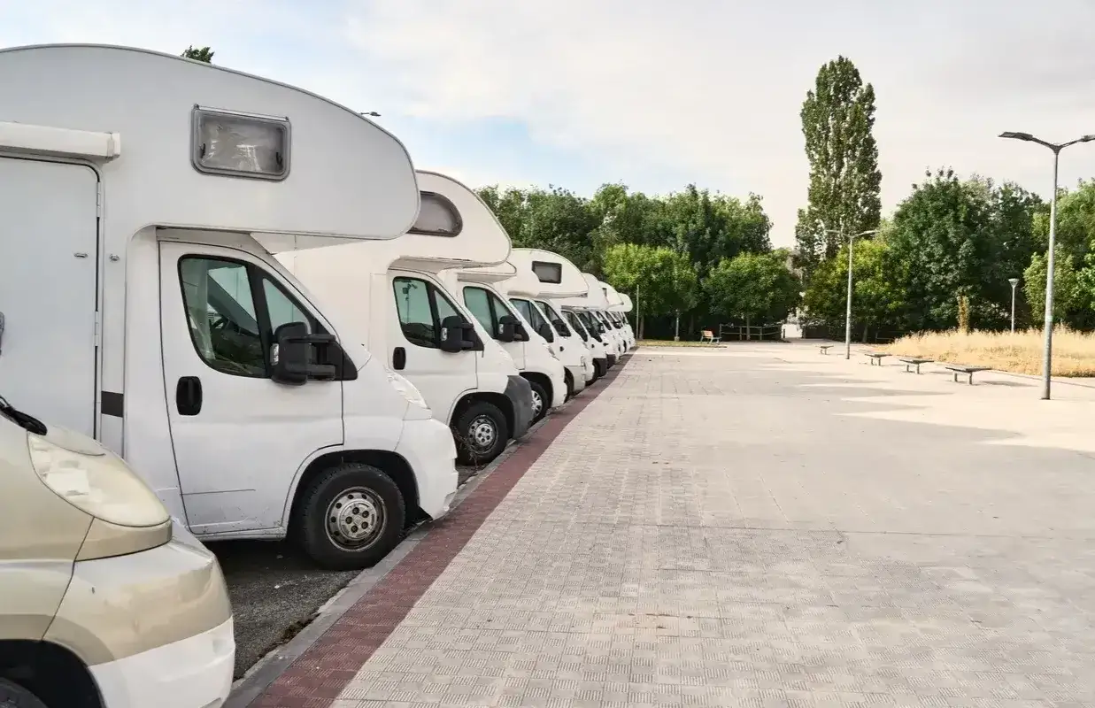 Fila de autocaravanas blancas aparcadas en un área de descanso.