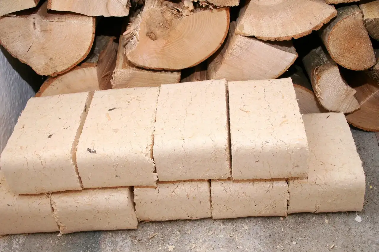 Holzbriketts, die man im Kaminofen verbrennen kann, liegen gestapelt neben gespaltenem Brennholz.