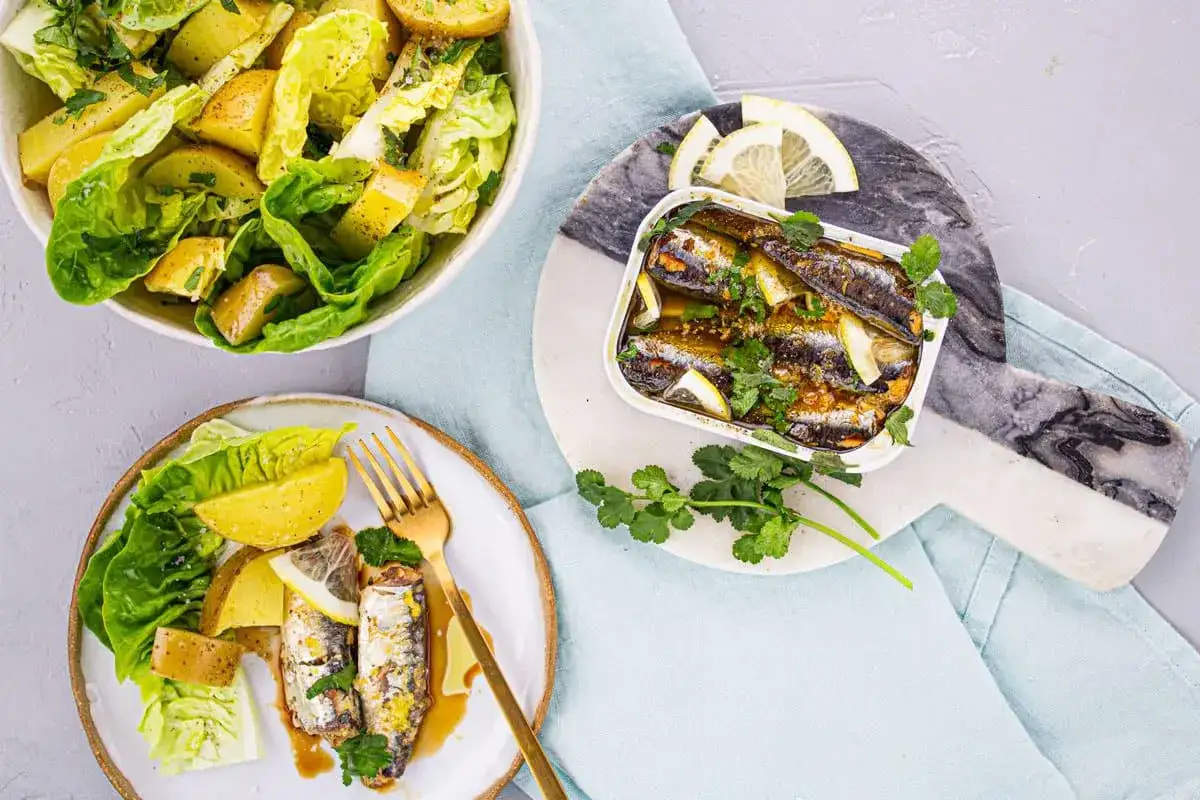 Sardines au four, dor&eacute;es et savoureuses, servies avec des quartiers de citron et une salade de pommes de terre et laitue croquante.