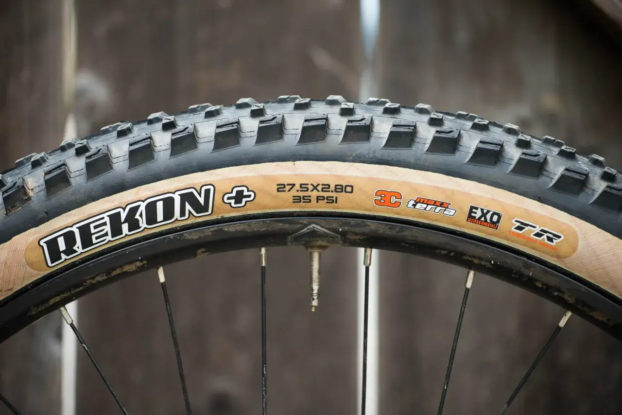 Close-up of a Maxxis Rekon+ tire with tan sidewalls, ready for trail riding. These tires are great for all-mountain adventures, as many Maxxis Rekon reviews suggest.