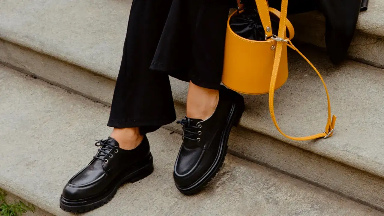 Come abbinare le stringate femminili: look audace con pantaloni neri e borsa gialla.