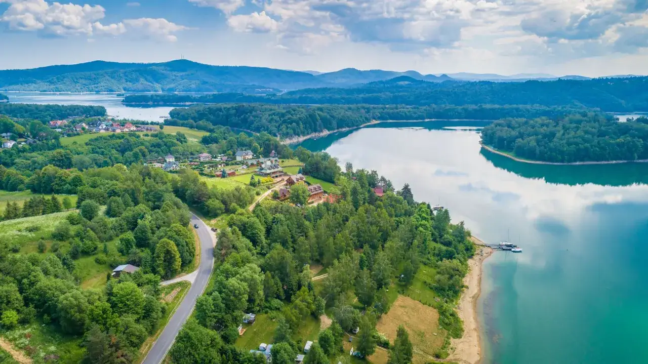 Bieszczady co warto zobaczyć: malownicza panorama z jeziorem, lasami i zabudowaniami. Idealne miejsce na wypoczynek.