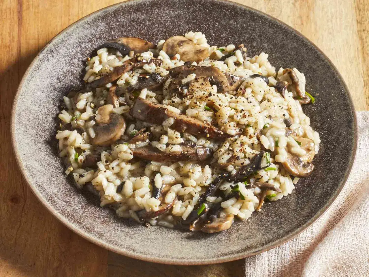 Un cremoso risotto de setas, con champiñones salteados y hierbas frescas, servido en un plato rústico.