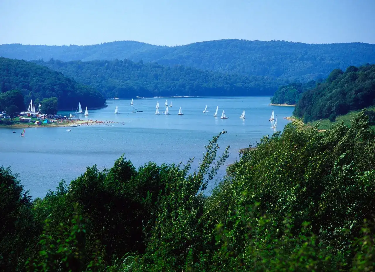 Idealne miejsce na wycieczkę 3 dniową: jezioro z żaglówkami, plażą i zielonymi wzgórzami w tle.