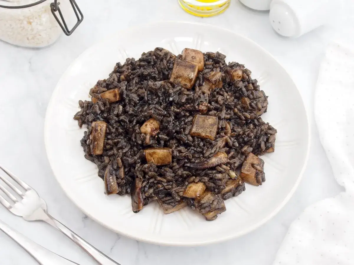 Arroz negro con sepia, un plato oscuro y sabroso, servido en un plato blanco con cubiertos.