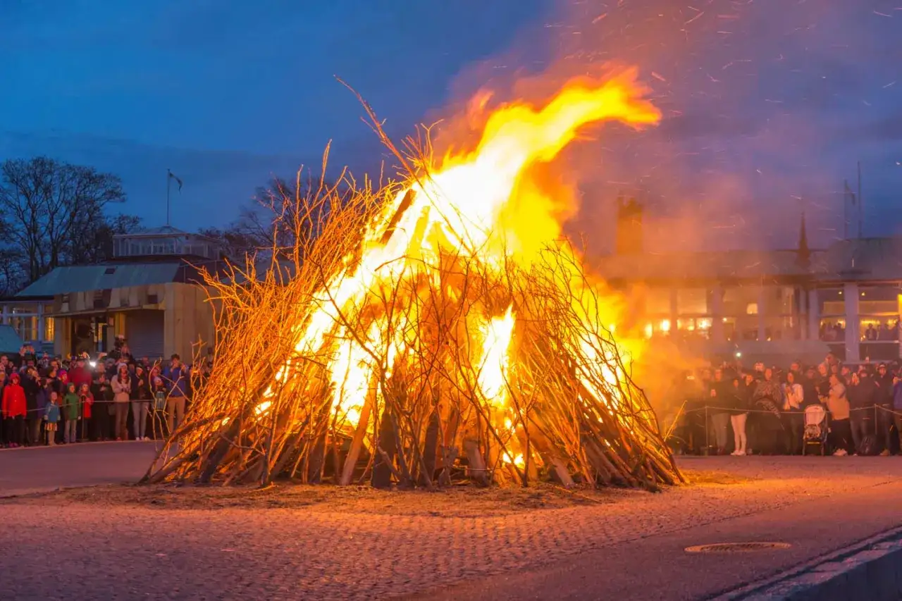Ett stort bål flammar upp under ett valborgsfirande. Människor samlas för att se på elden och fira vårens ankomst.