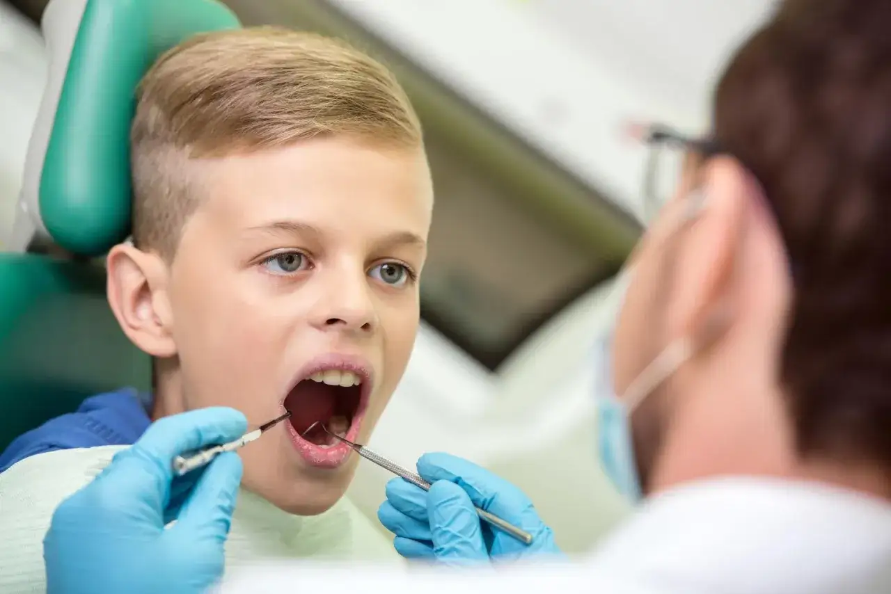 Chłopiec z otwartymi ustami podczas wizyty u dentysty. Lekarz bada jego zęby, sprawdzając, czy nie ma kłykcin w jamie ustnej.