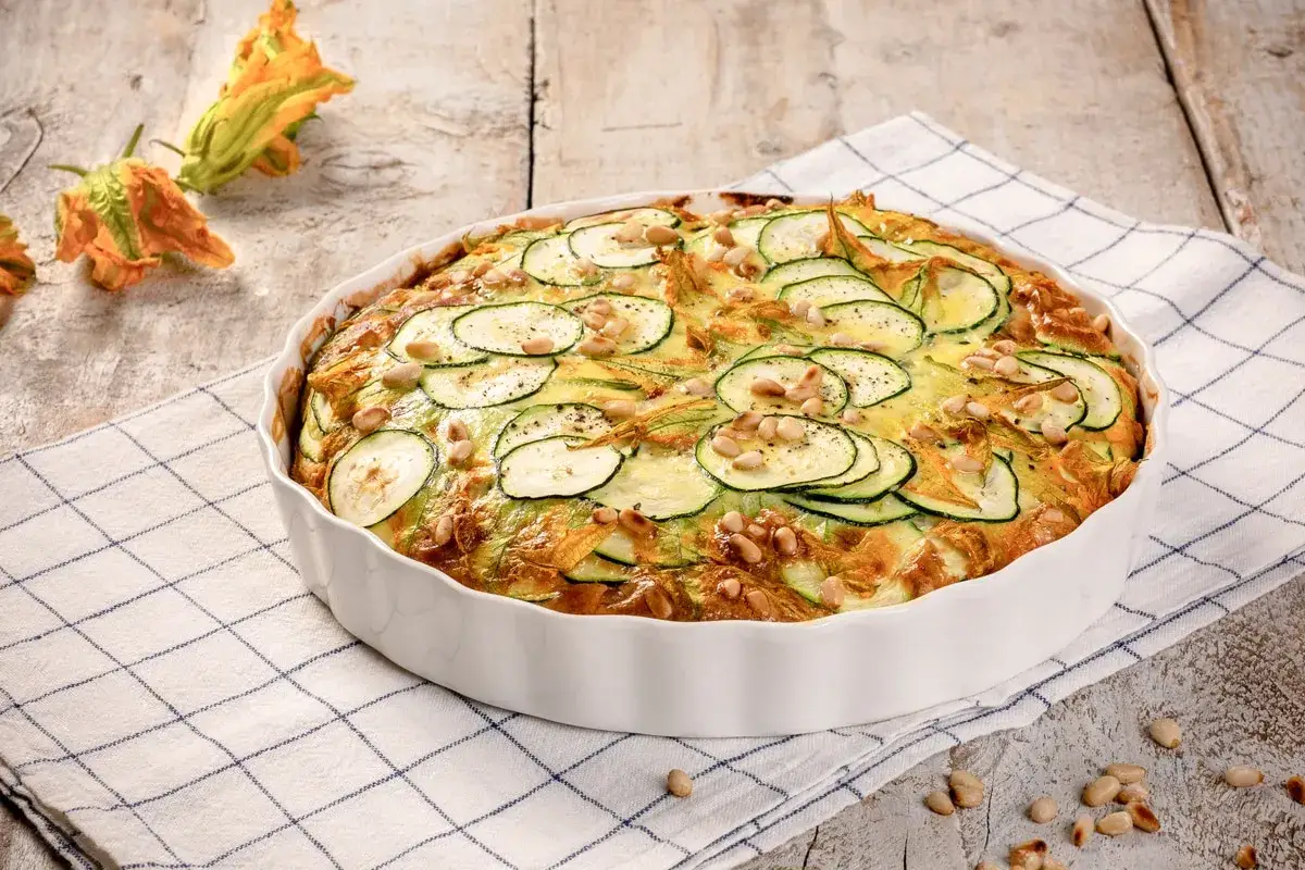 Deliziosa frittata di zucchine al forno, guarnita con pinoli e fiori di zucca, pronta per essere gustata.