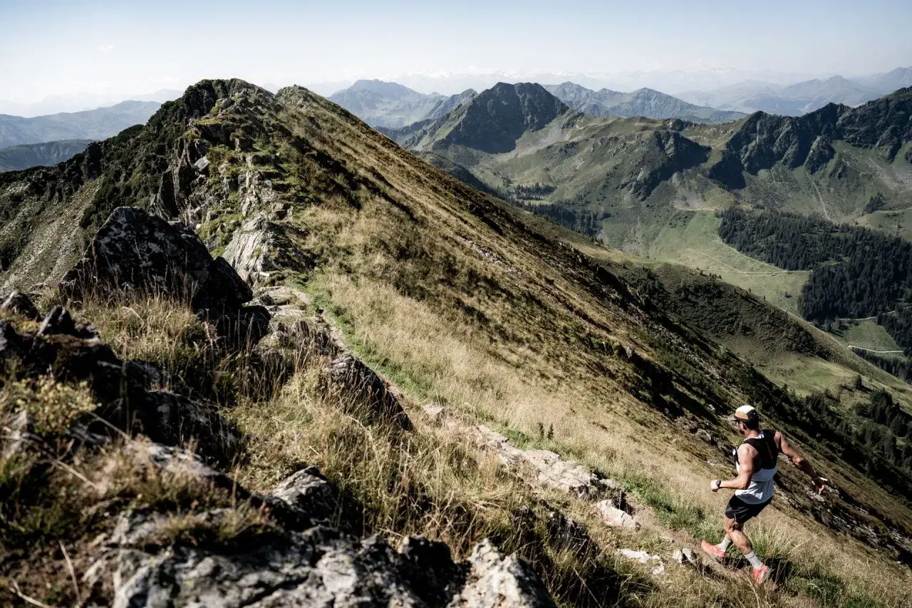 Un coureur affronte le sentier escarp&eacute; du kat100 by utmb, dominant un paysage montagneux spectaculaire.
