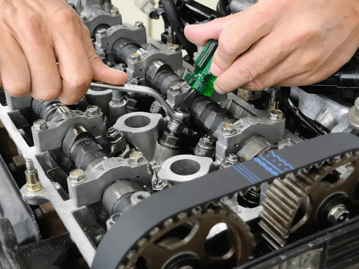 Mechanik reguluje luz zaworowy silnika, używając klucza i śrubokręta.