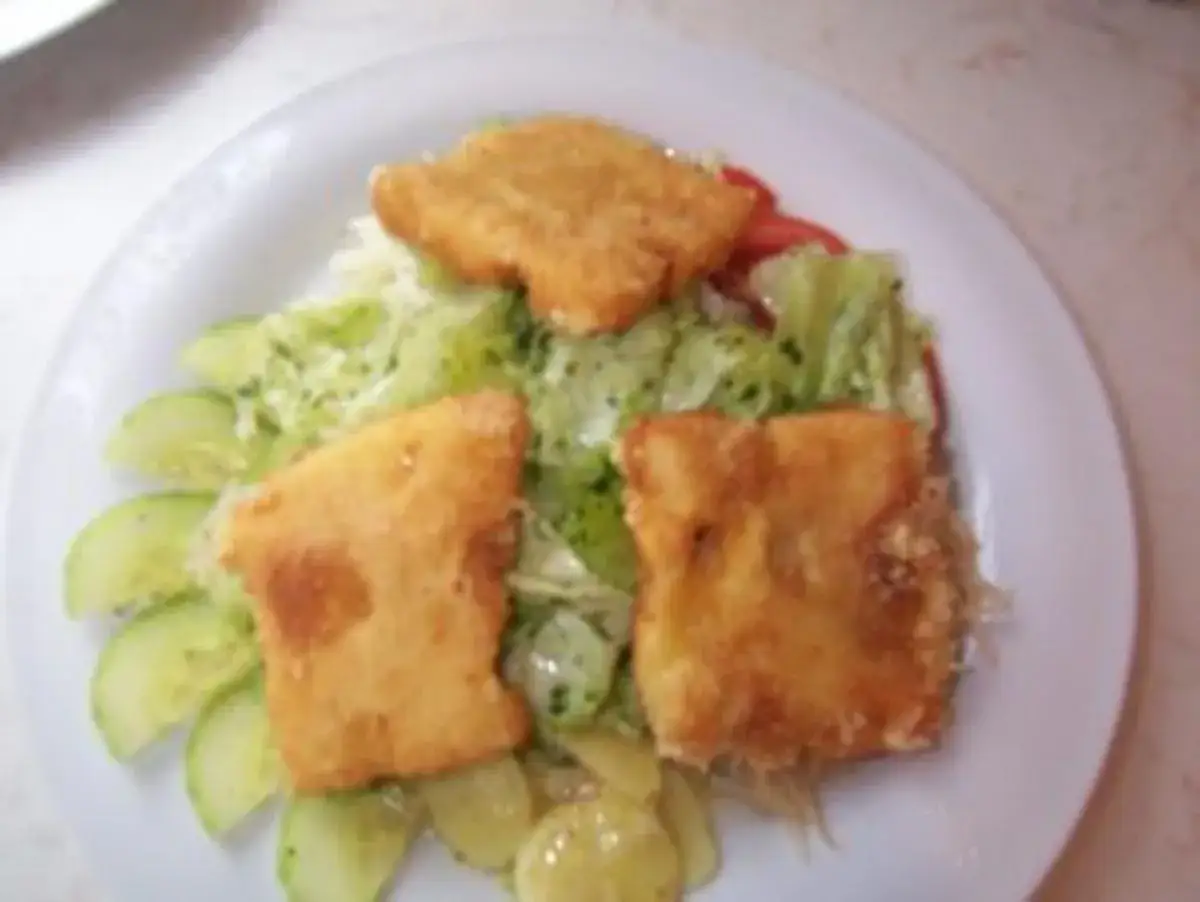 Drei goldbraun gebackene Emmentaler-Schnitzel auf einem Salatbett mit Gurkenscheiben und Tomaten.