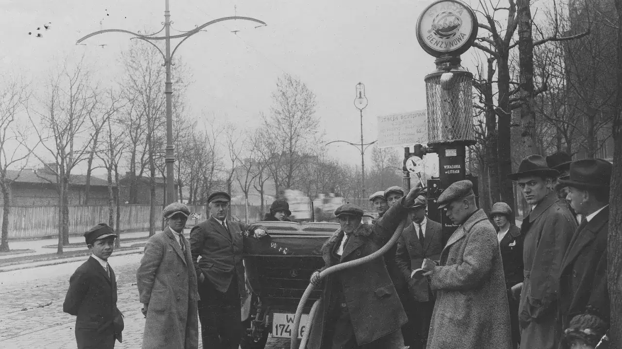 Mężczyźni tankują samochód na stacji benzynowej. Widać dystrybutor z napisem