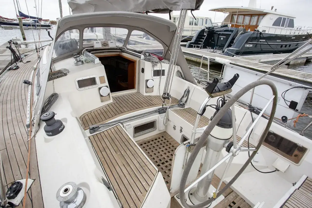 Cockpit d'un voilier blanc avec des sièges en teck et un grand volant. Derrière, d'autres bateaux sont amarrés. Les premiers 375 avis sont positifs.