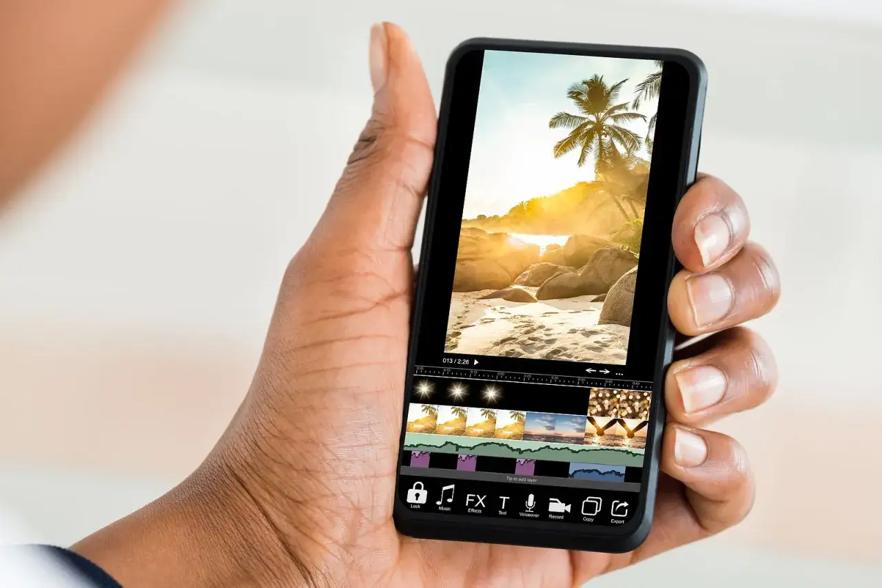 Mano sujetando un smartphone con un editor de fotos Android, mostrando una playa tropical al atardecer y opciones de edici&oacute;n.