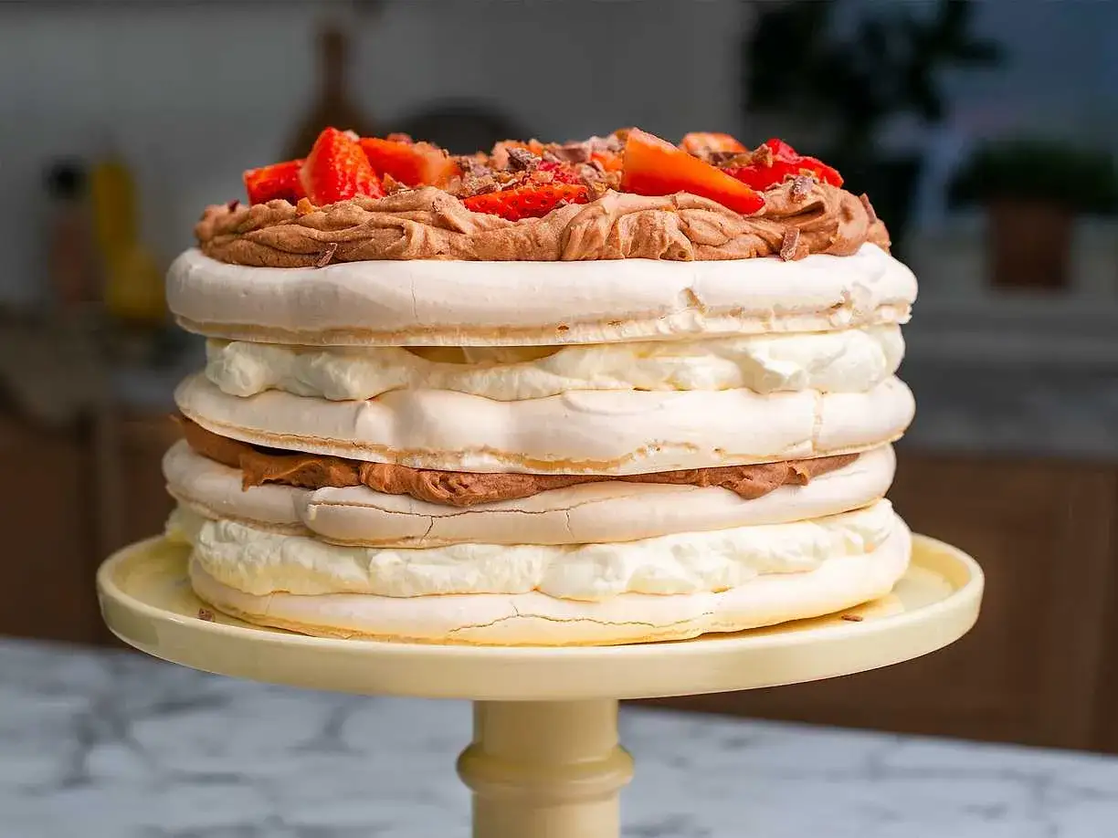 En imponerande **Daim tårta** med marängbottnar, fluffig grädde och chokladkräm, toppad med färska jordgubbar och krossad Daim.