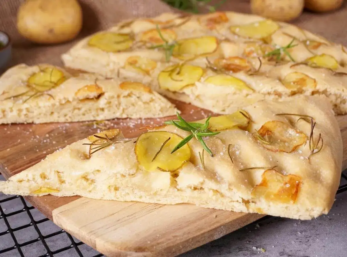 Eine köstliche Kartoffel-Focaccia mit Rosmarin und grobem Salz, auf einem Holzbrett serviert.