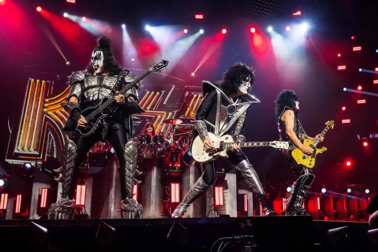 Les membres du groupe KISS, maquillés et costumés, jouent sur scène. Le chanteur au centre tient une guitare blanche.