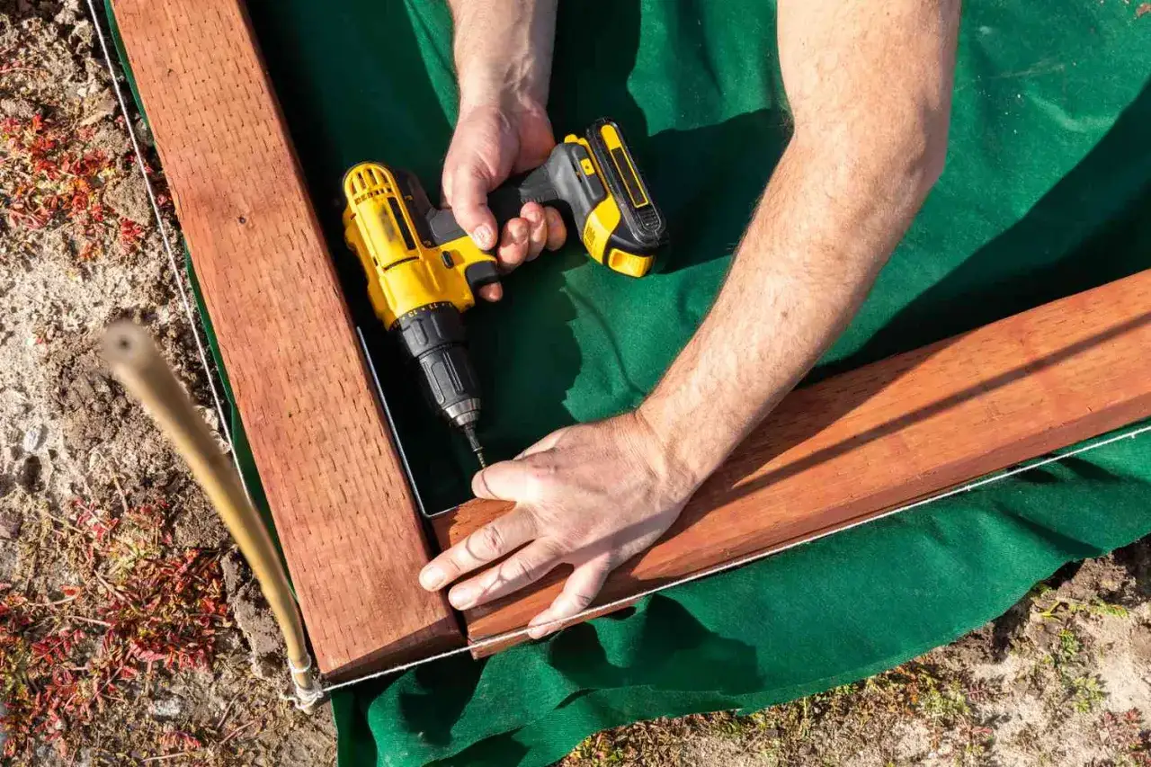 Hands use a yellow drill to attach landscape timbers, demonstrating how to install them for a garden bed.