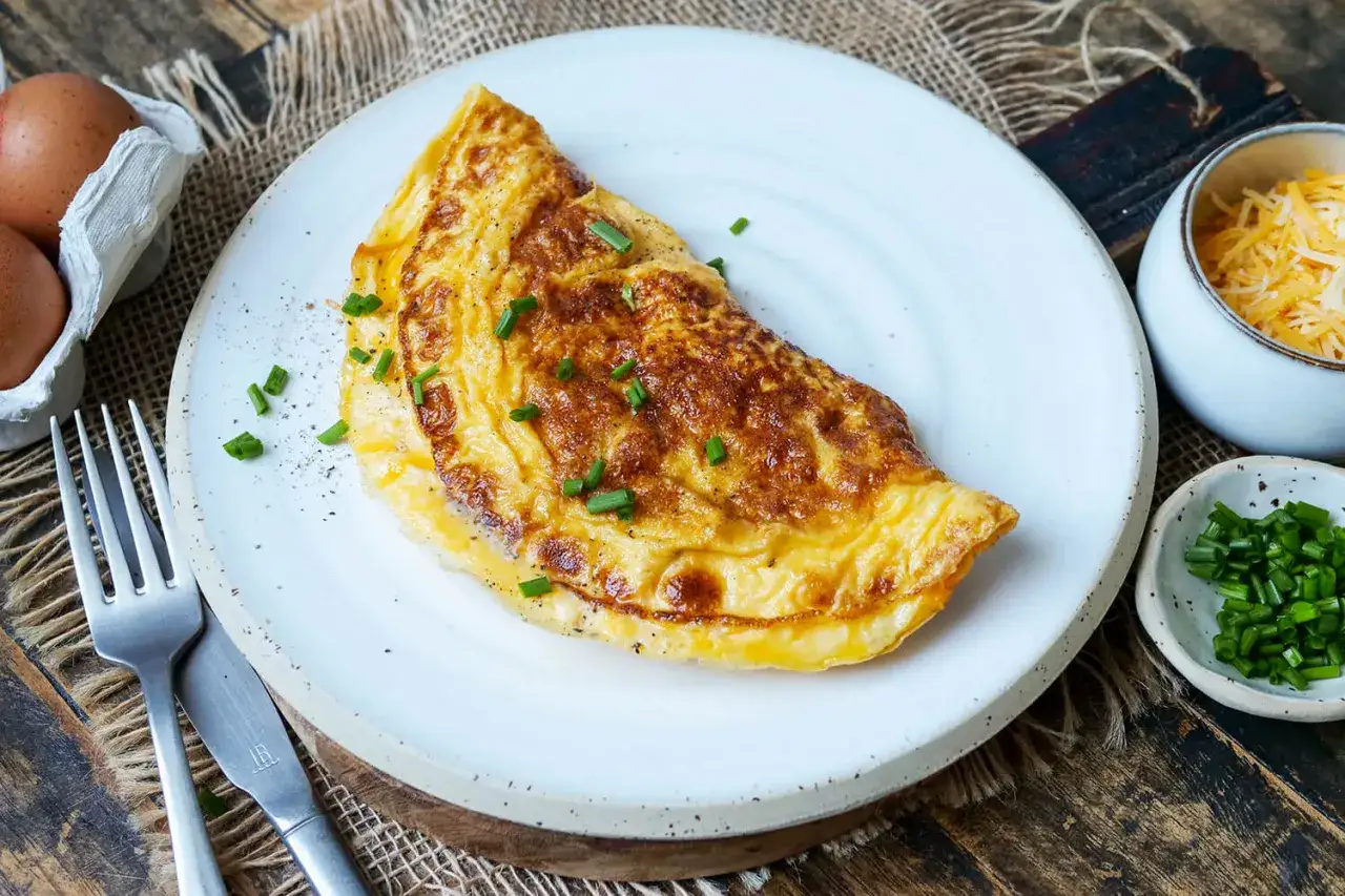 Goldbraunes Omelett mit Käse und Schnittlauch, perfekt für ein schnelles Omelett Rezept. Daneben Eier, Käse und Schnittlauch.