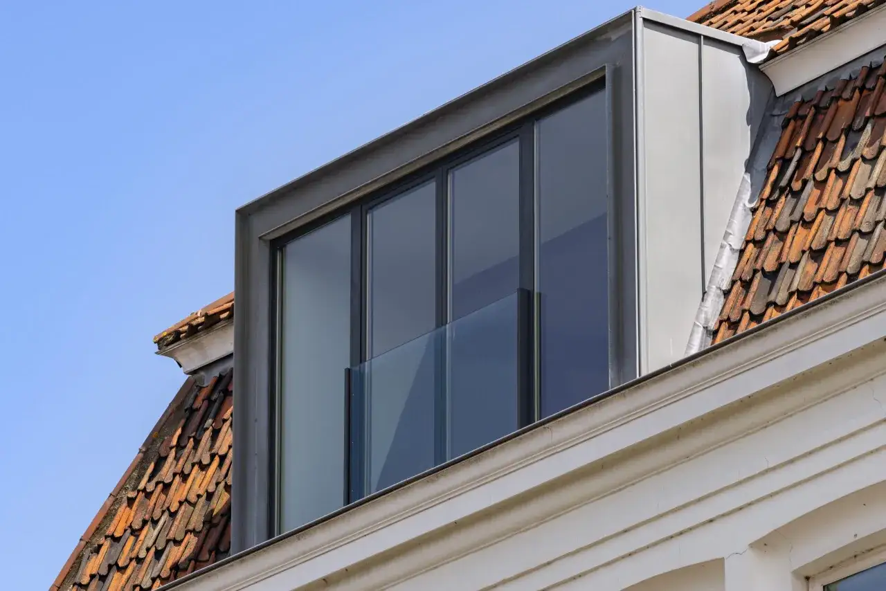 Moderne dakkapel met grote ramen, een glazen balustrade en zinken afwerking. Dit toont aan wat is prefab: een efficiënte bouwmethode.
