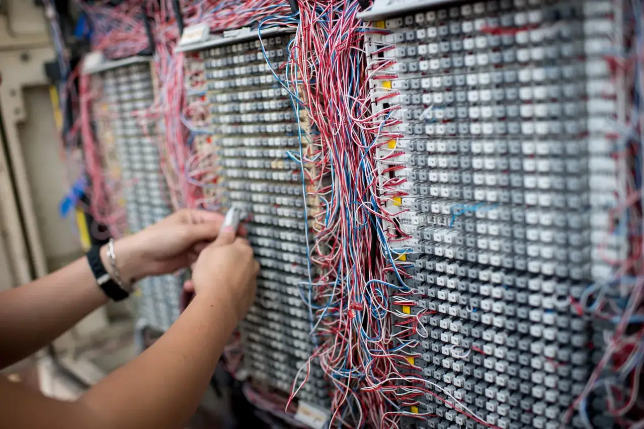 Une personne manipule un panneau de connexions t&eacute;l&eacute;phoniques. Comprendre le VDSL, c'est comprendre comment ces fils acheminent les donn&eacute;es.