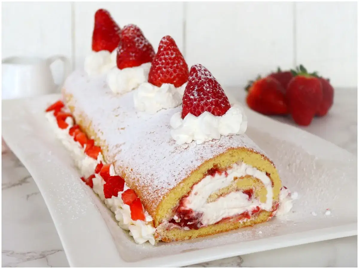 Delizioso rotolo panna e fragole, spolverato di zucchero a velo e decorato con fragole fresche. Un dolce invitante.