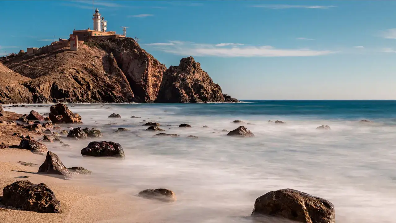 Faro en un acantilado rocoso sobre el mar, con rocas en la playa. Un lugar idílico que ver en Cabo de Gata.