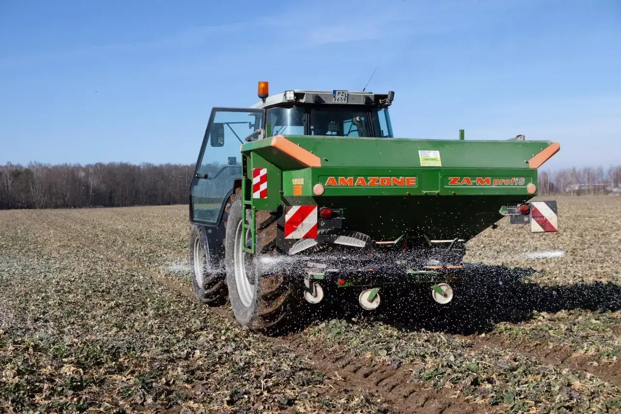 Traktor z rozsiewaczem Amazone ZA-M profis na polu, rozsypuje naw&oacute;z. Rolnik dba o to, ile owsa na hektar będzie miał w przyszłości.