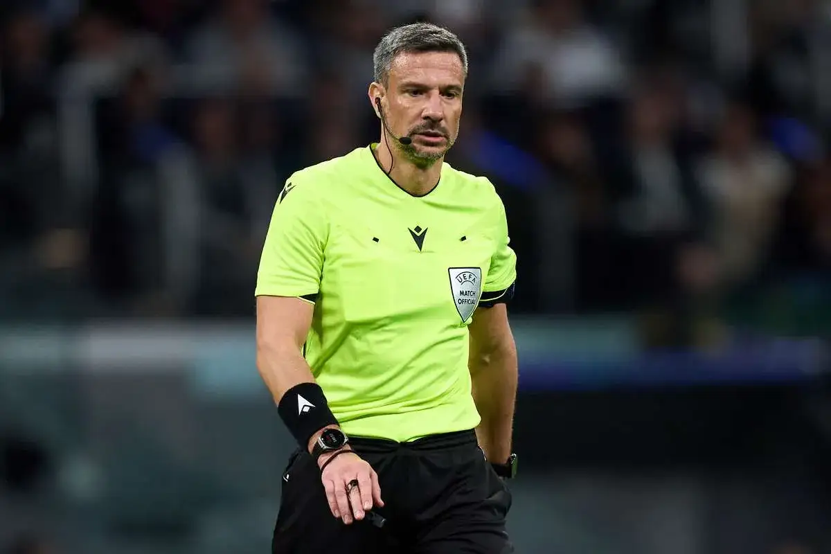 Sędzia piłkarski w jaskrawej koszulce z logo UEFA, skupiony na boisku.