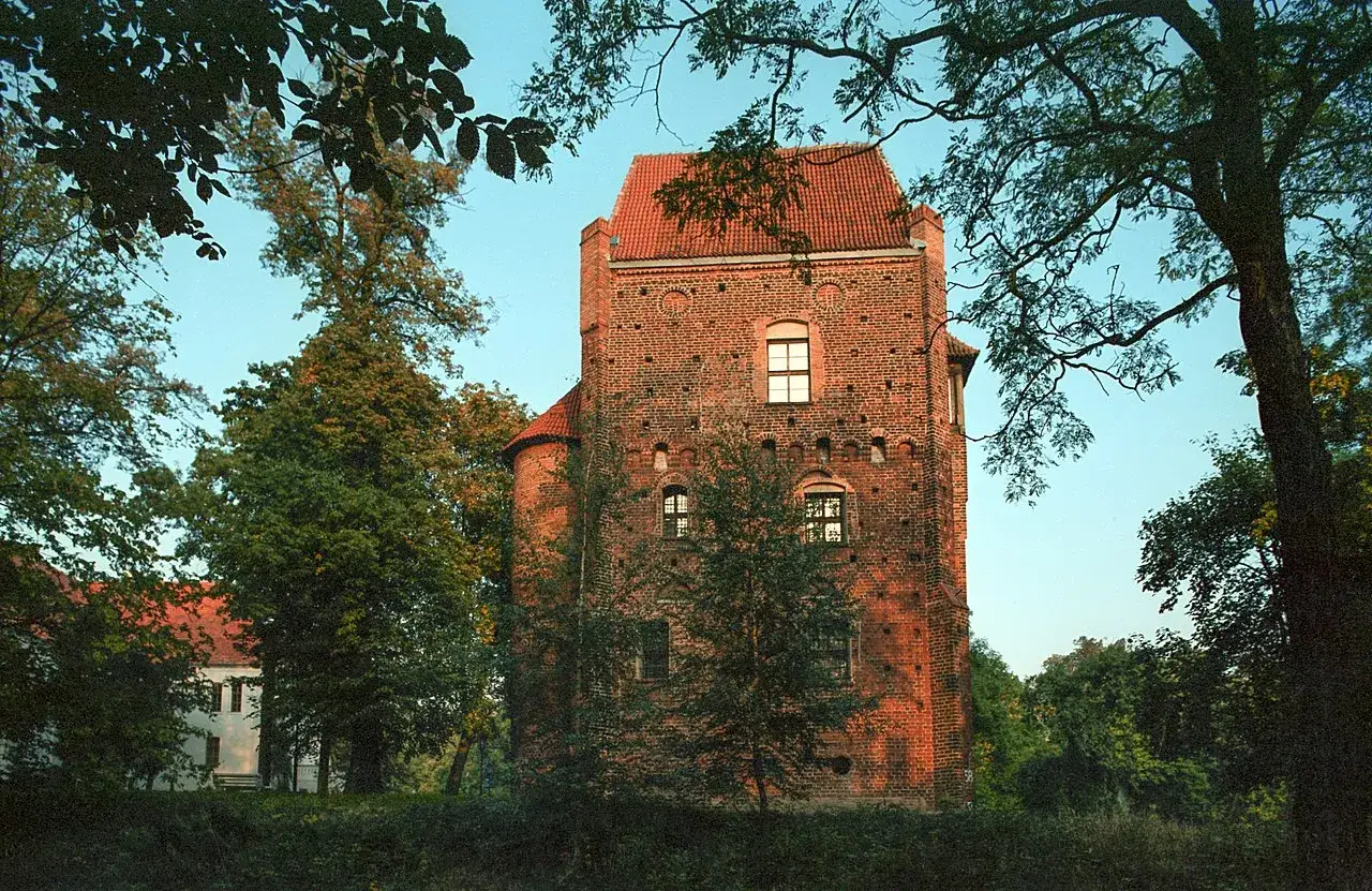 Zamek Górków, ceglana wieża z czerwonym dachem, otoczona zielenią drzew.