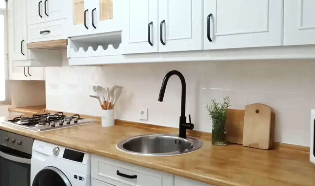 Cocina moderna con muebles de melamina blancos, encimera de madera y grifería negra. Ideal para renovar tus muebles de cocina de melamina.