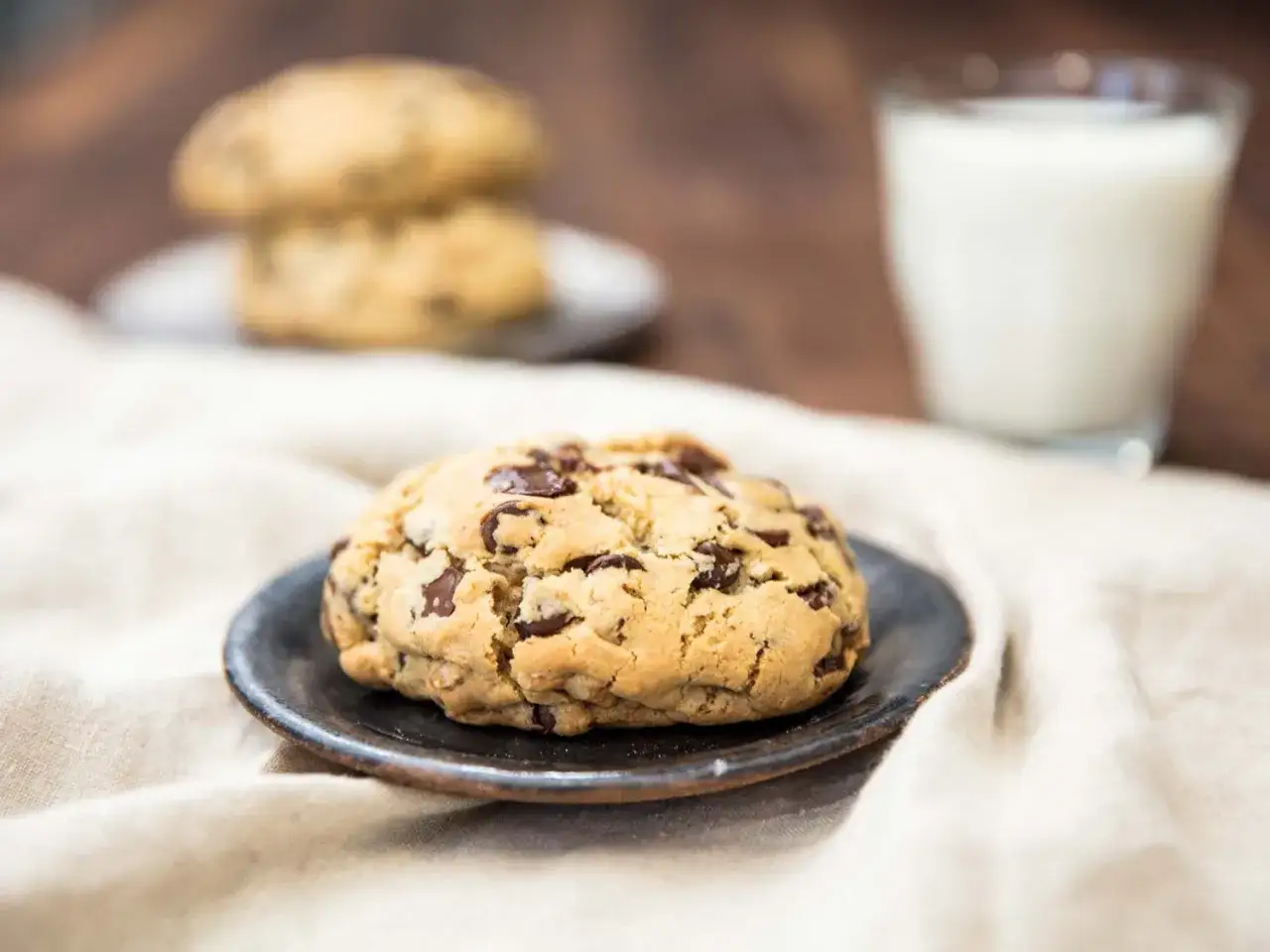 Saftige american cookies backen ist eine Kunst. Hier ein frisch gebackener Chocolate Chip Cookie auf einem Teller, daneben ein Glas Milch.
