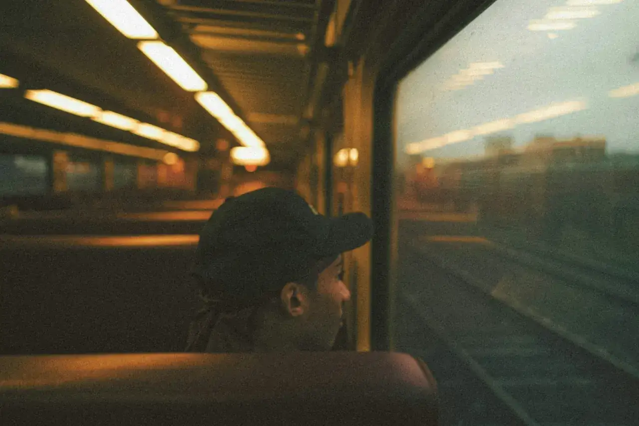 Persona con gorra mira por la ventana de un tren, como si soñara con el viaje.