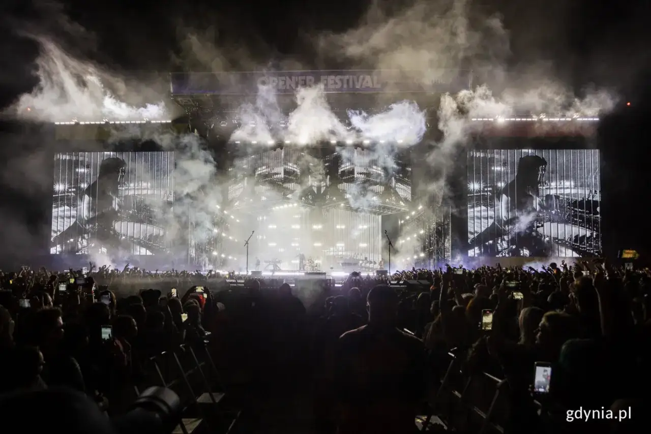Koncert Linkin Park na Open'er Festival. Tłum ludzi z telefonami w górze, dym i światła na scenie.