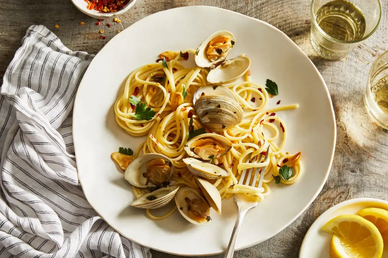 En tallrik med spaghetti vongole, toppad med f&auml;rska musslor, vitl&ouml;k och persilja. En gaffel &auml;r redo att njuta av denna klassiska italienska r&auml;tt.