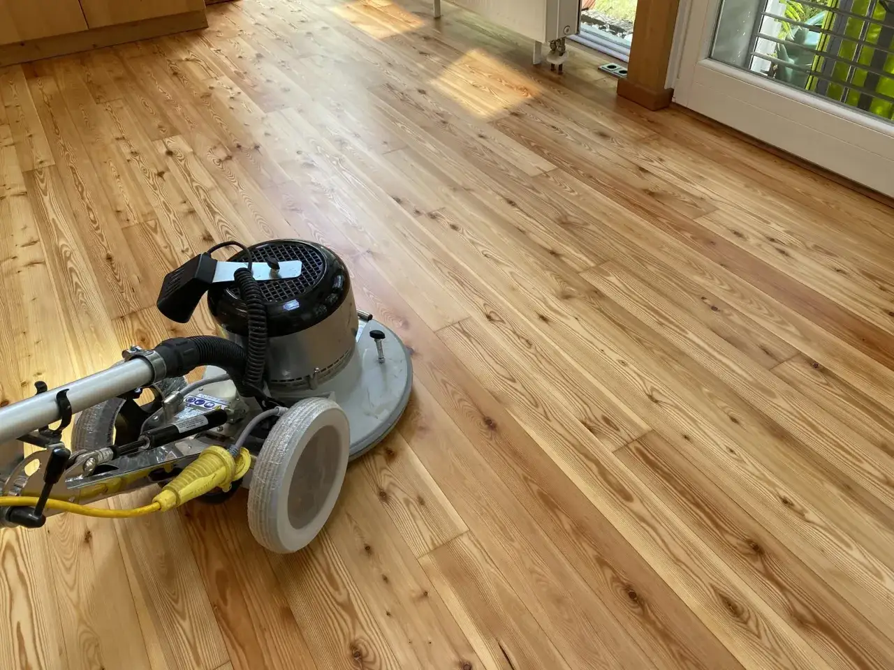 Maschine zum Parkett versiegeln steht auf hellem Holzboden. Sonnenlicht f&auml;llt auf die Dielen.